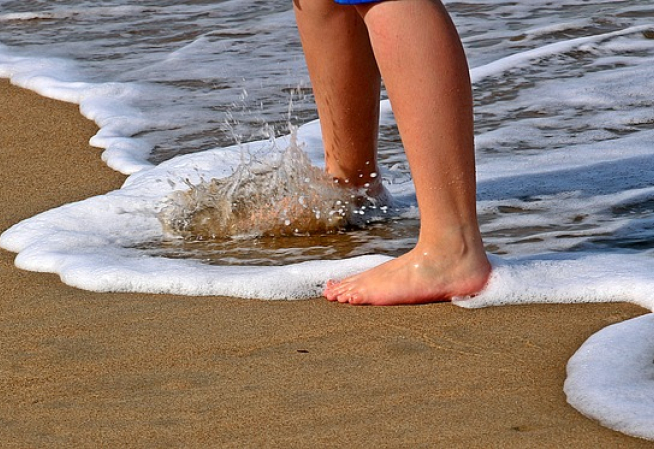 pieds d'un enfant au bord de l'eau sur une plage